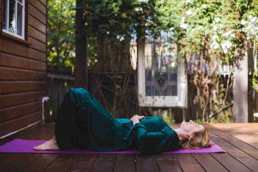 Sarah Tuckett Somatic Psychotherapy Brisbane performing a somatic therapy technique lying on a yoga mat on a deck, surrounded by greenery