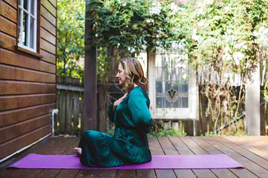 Sarah Tuckett Somatic Psychotherapy Brisbane sitting on a purple yoga mat on her deck, demonstrating how to listen to your body